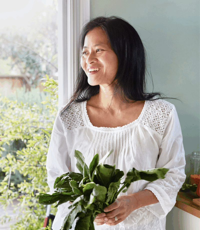 Chef Linda Shiue holding a bunch of basil standing next to a window