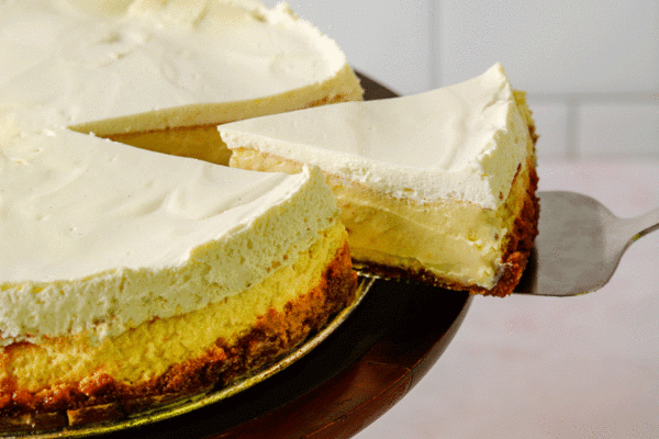 Slice of lemon cheesecake lifted out of full cheesecake on cake stand