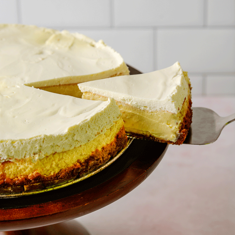 Slice of lemon cheesecake lifted out of full cheesecake on cake stand