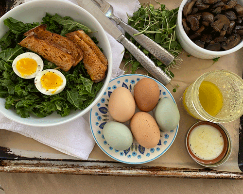 Salad with cooked egg and croutons and a bowl of colorful eggs and a jar of viniagrette