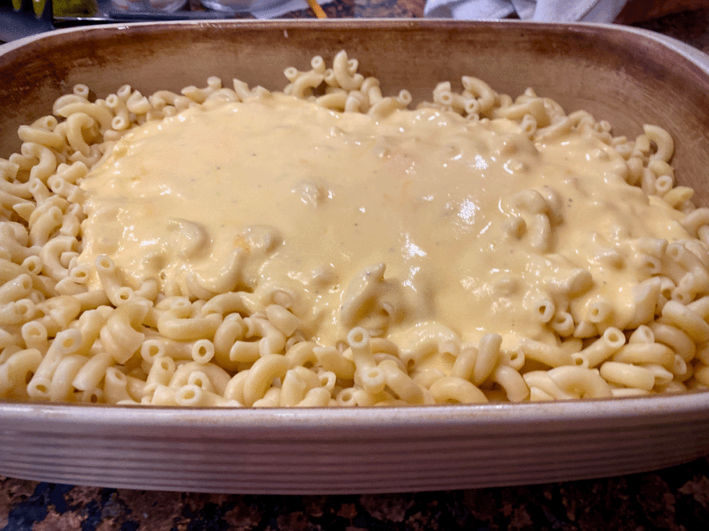Cheese sauce poured over cooked elbow macaroni in a casserole