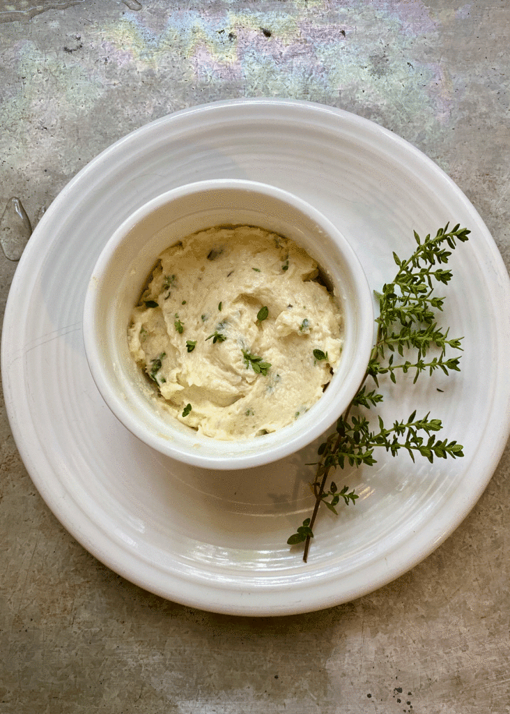 Horseradish-thyme butter in a bowl on a plate with a sprig of thyme
