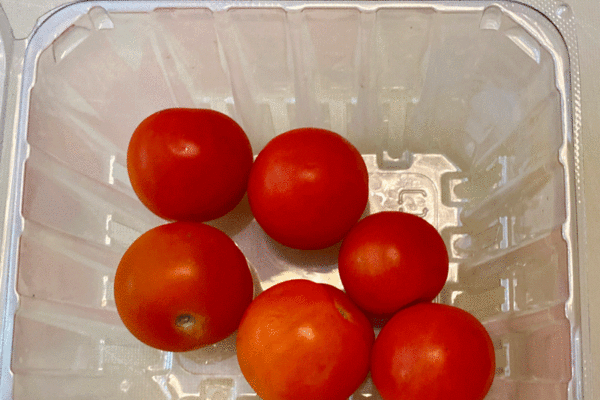 Cherry tomatoes in a plastic container on a cutting board