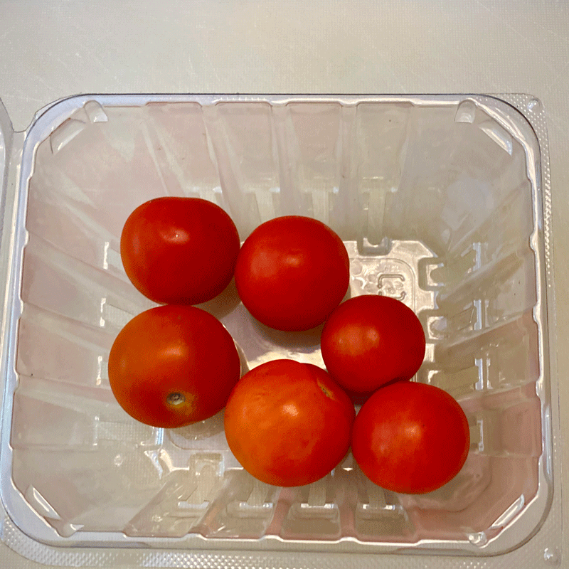 Cherry tomatoes in a plastic container on a cutting board