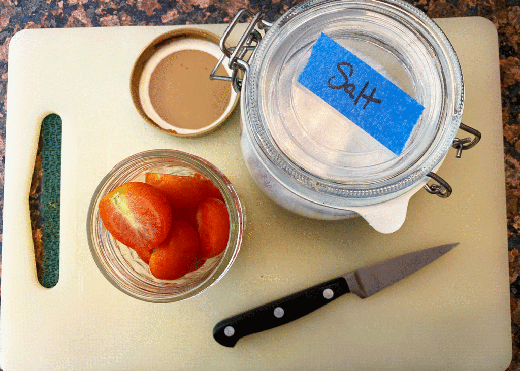Sliced tomatoes in a glass jar with salt and a knife on a cutting board