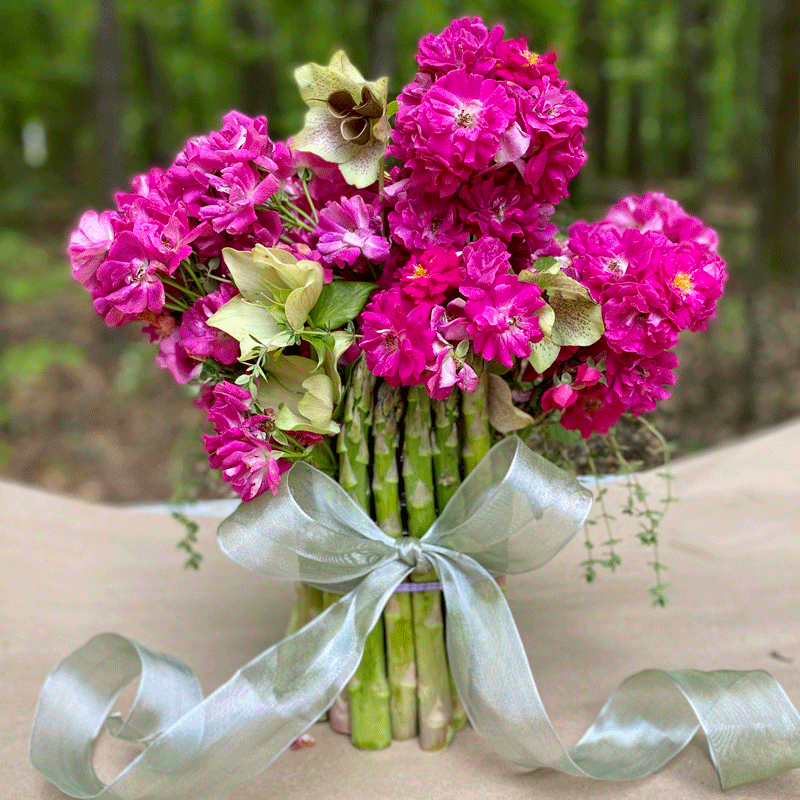 A vase made of asparagus with pink roses inside and tied with a ribbon