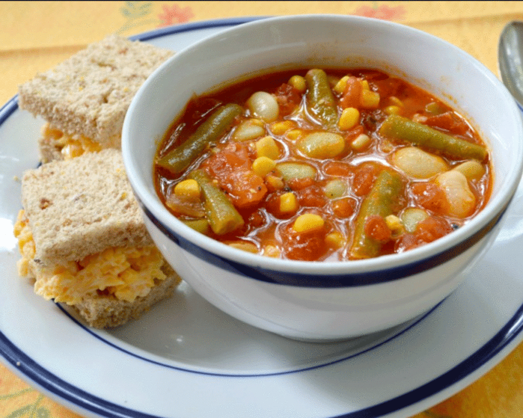 Vegetable soup in a bowl with pimento cheese sandwiches on a plate