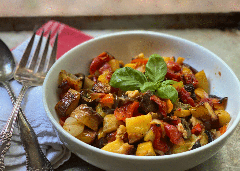 A bowl full of roasted vegetables with a spoon and fork on the side