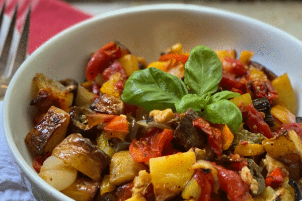 Roasted vegetables in a bowl with a sprig of basil
