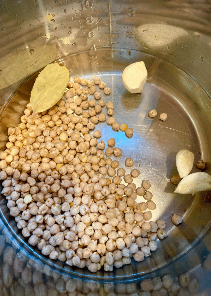 Dried chickpeas in an electric pressure cooker with garlic cloves and bay leaf
