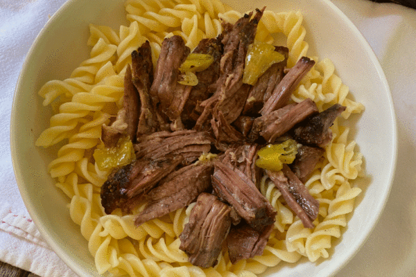 Shredded pot roast meat over noodles in a white bowl
