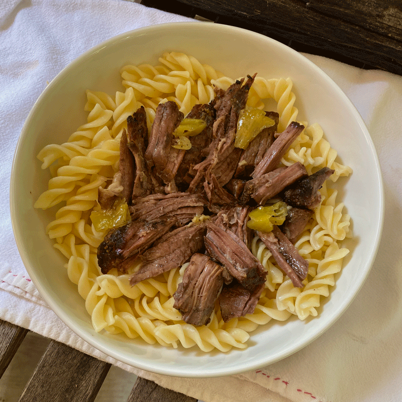 Shredded pot roast meat over noodles in a white bowl