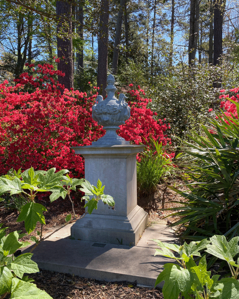 Statue in a garden with a background of blooming red azaleas