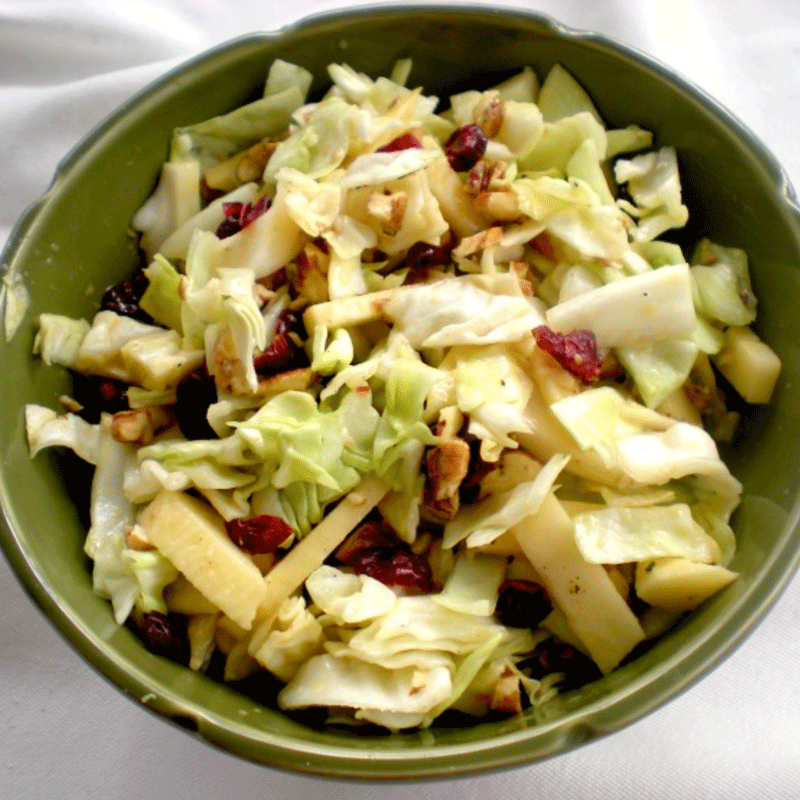 Green bowl with slaw made of cabbage, apples, pecans and cranberries