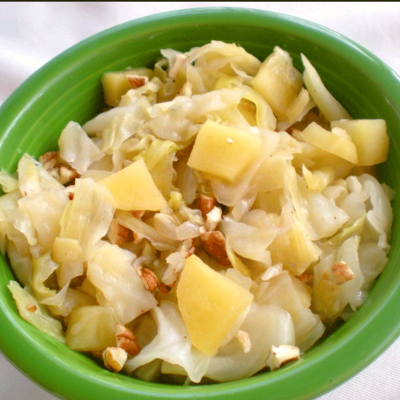 Cooked cabbage with apples and pecans in a green bowl