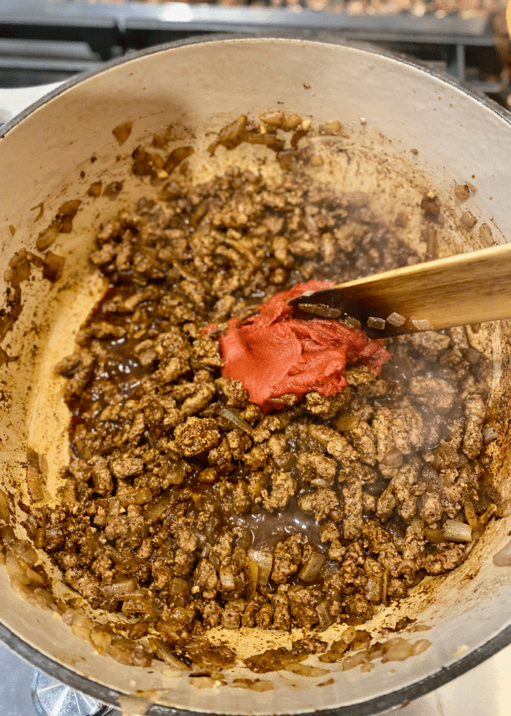 Stirring tomato paste into browned ground beef