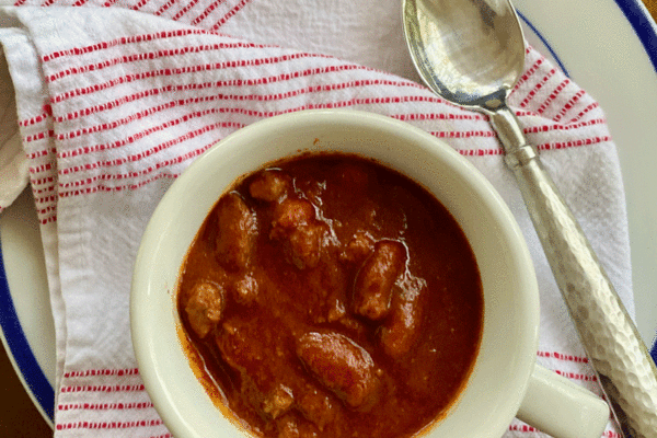 Chili in a white bowl with a spoon and napkin with red stripes