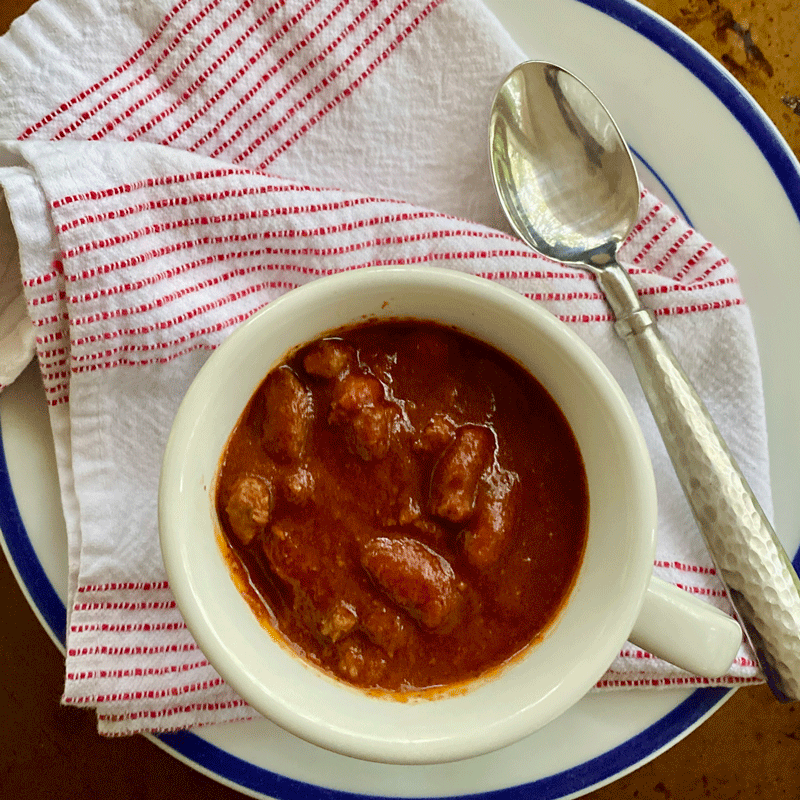 Chili in a white bowl with a spoon and napkin with red stripes