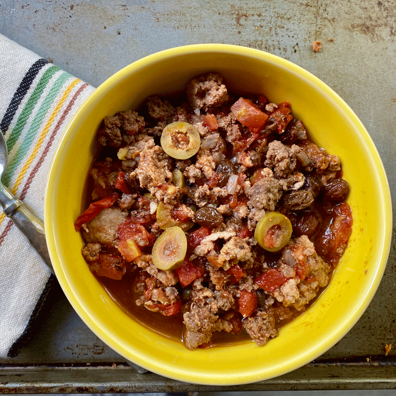 A bowl full of picadillo, seasoned ground meat with olives and raisins