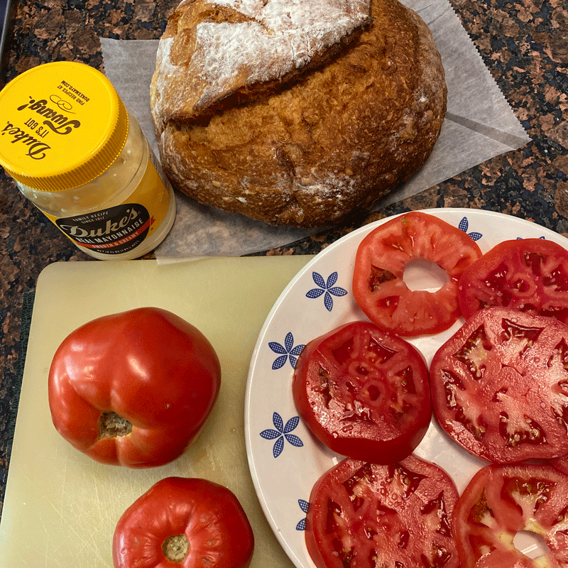 Ingredients for a tomato sandwich on a cutting board in a kitchen