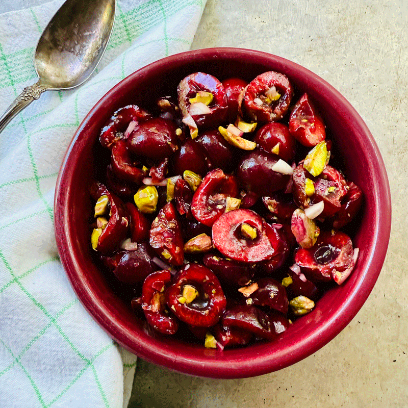 Cherry salad with pistachios in a red bowl on a green napkin with a silver spoon