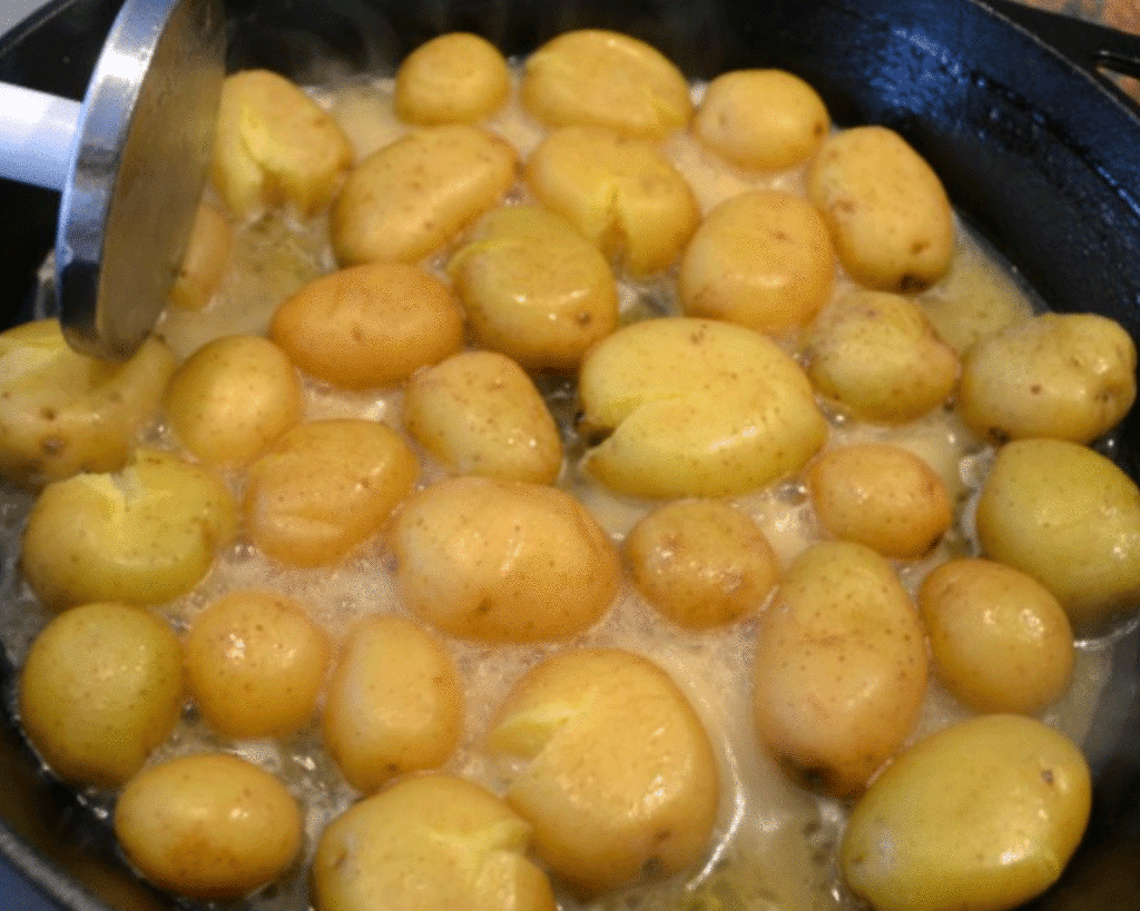 Potatoes roasting in a cast iron pan while a cook holds a meat pounder