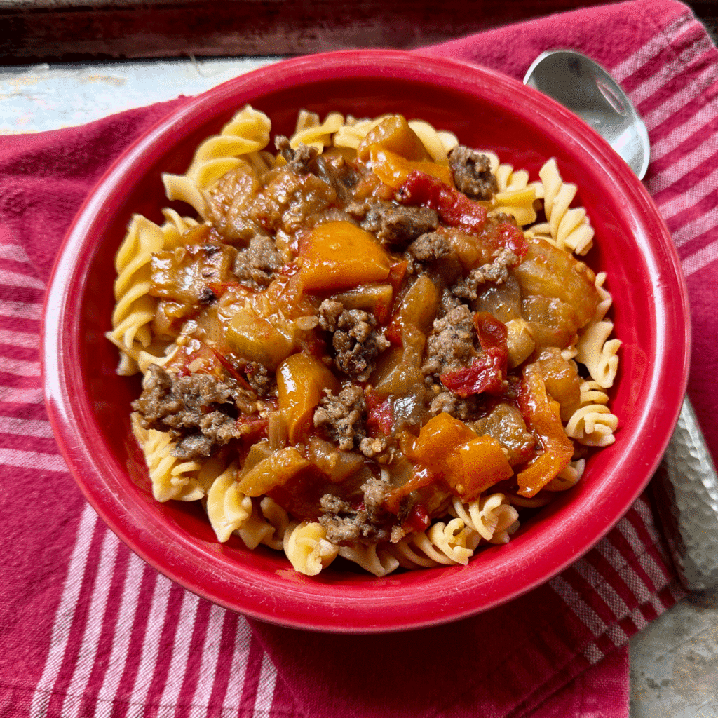 A red bowl filled with ratatouille served over pasta