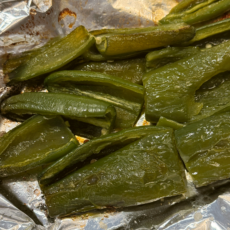 Roasted jalapeno peppers on a foil-lined baking sheet