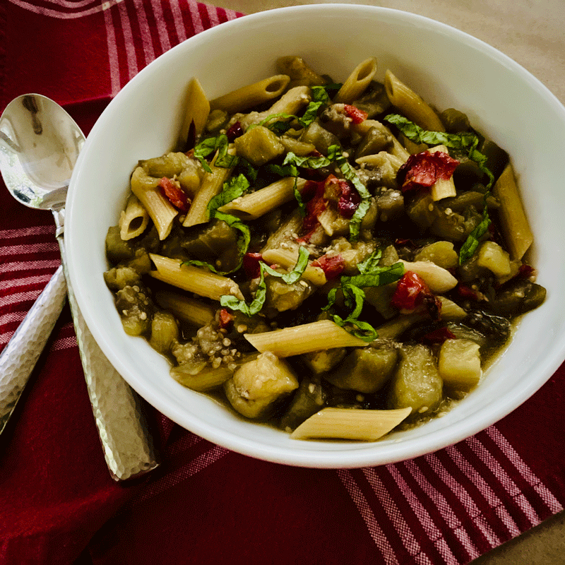 Eggplant pasta in bowl on a placemat with fork and spoon