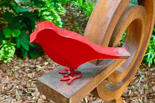 A metal sculpture of a bird painted red in a garden