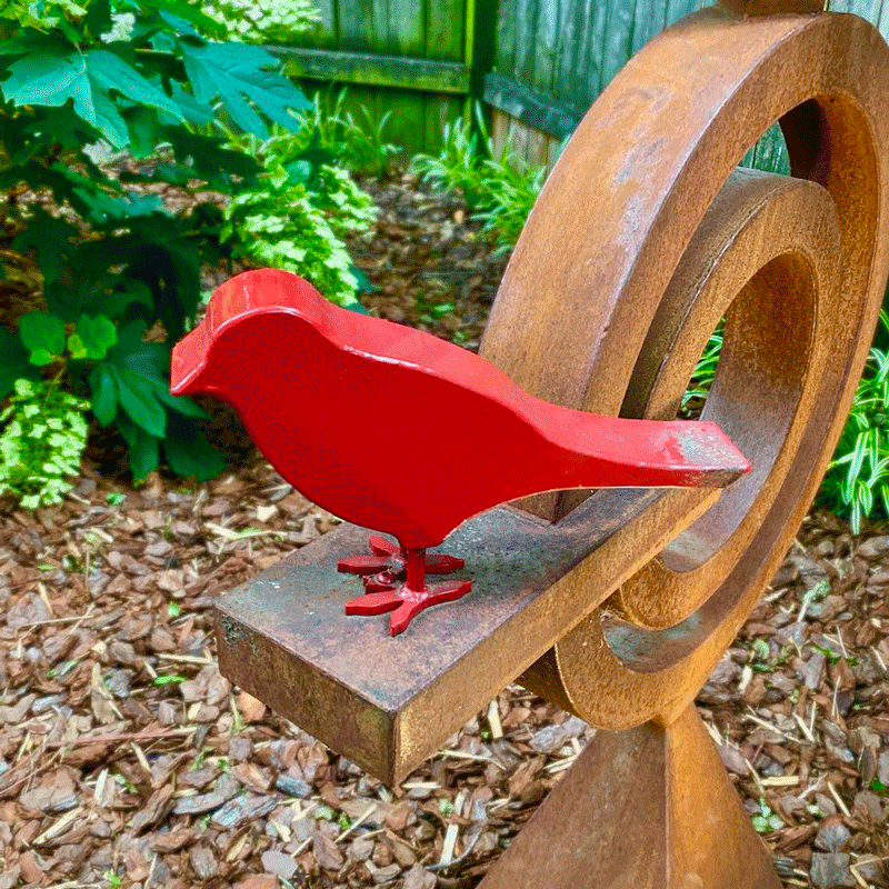 A metal sculpture of a bird painted red in a garden