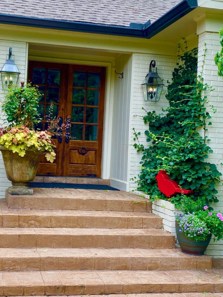 A home entrance with a red metal bird sculpture and flower planters
