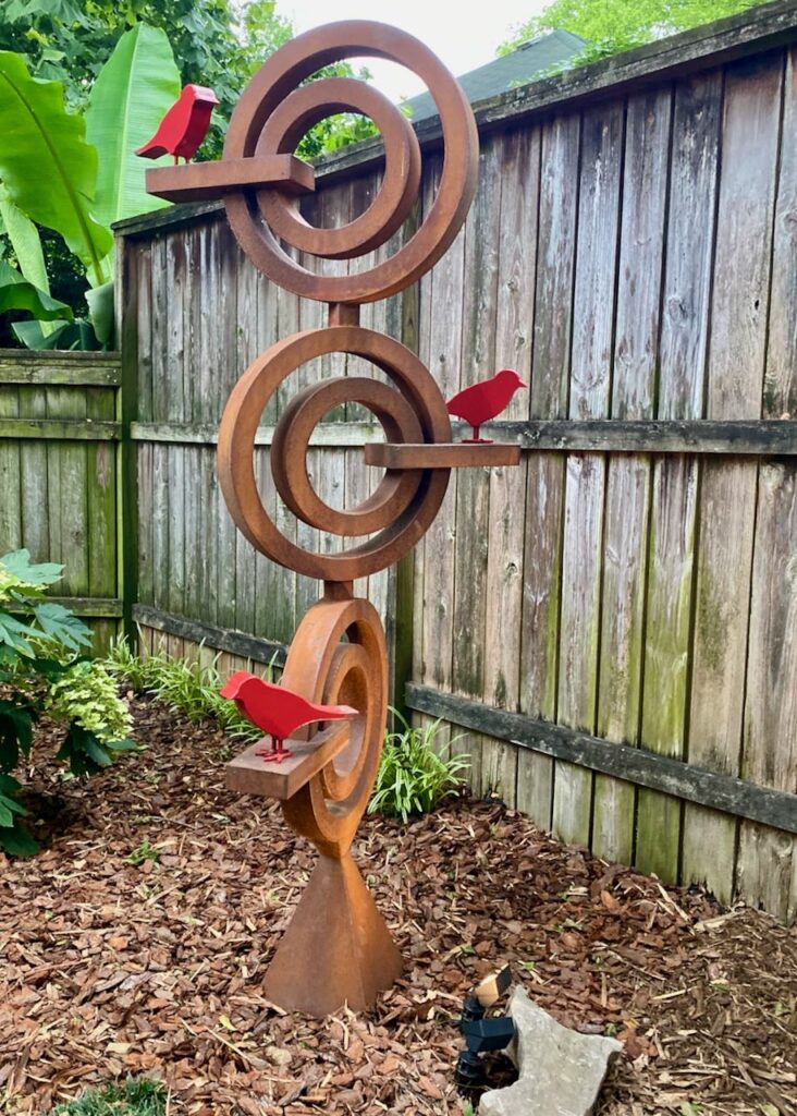 A metal sculpture with three red birds in a garden