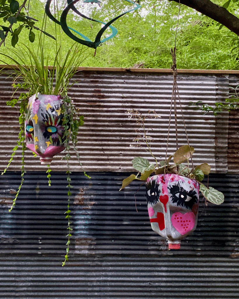 Painted milk jug planters hanging from a tree in a garden