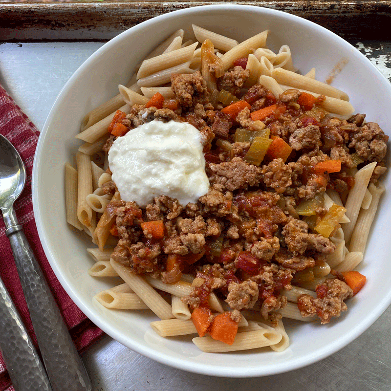 Bowl of penne pasta topped with ground turkey meat sauce and ricotta